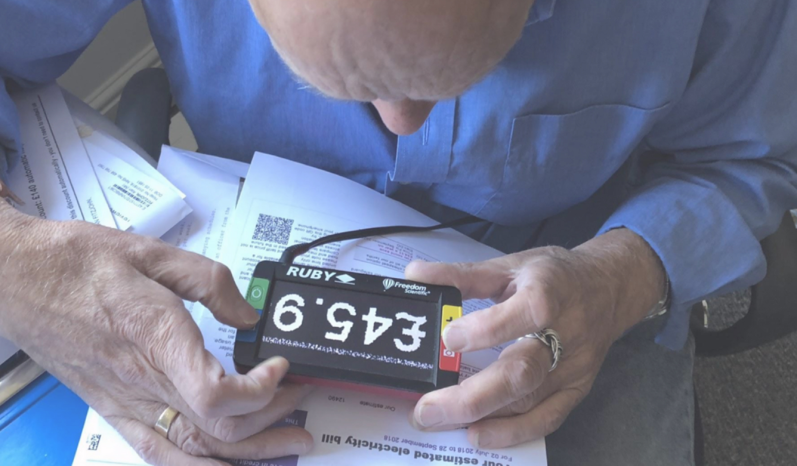 a photograph of a man reading his energy bill with assistive technology to zoom in.